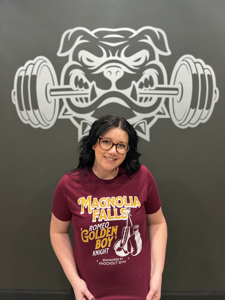 a woman standing in front of a wall wearing a maroon shirt