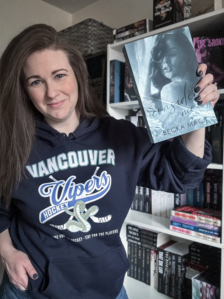 a woman holding up a book in front of a bookshelf