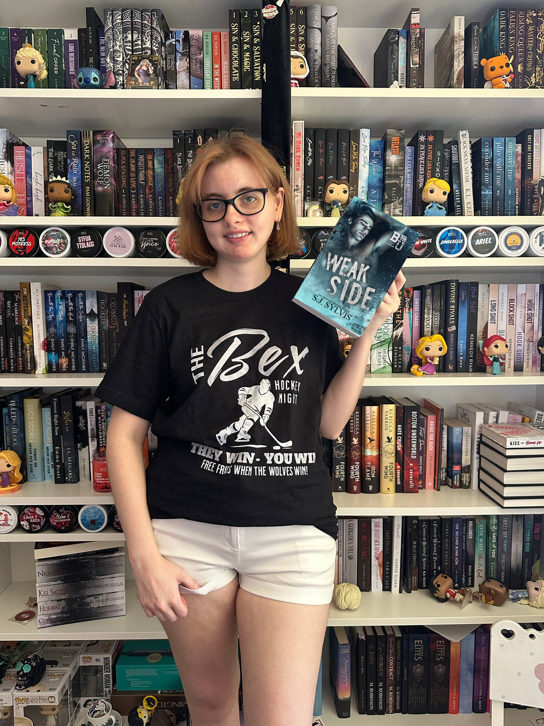 a woman standing in front of a book shelf holding a book