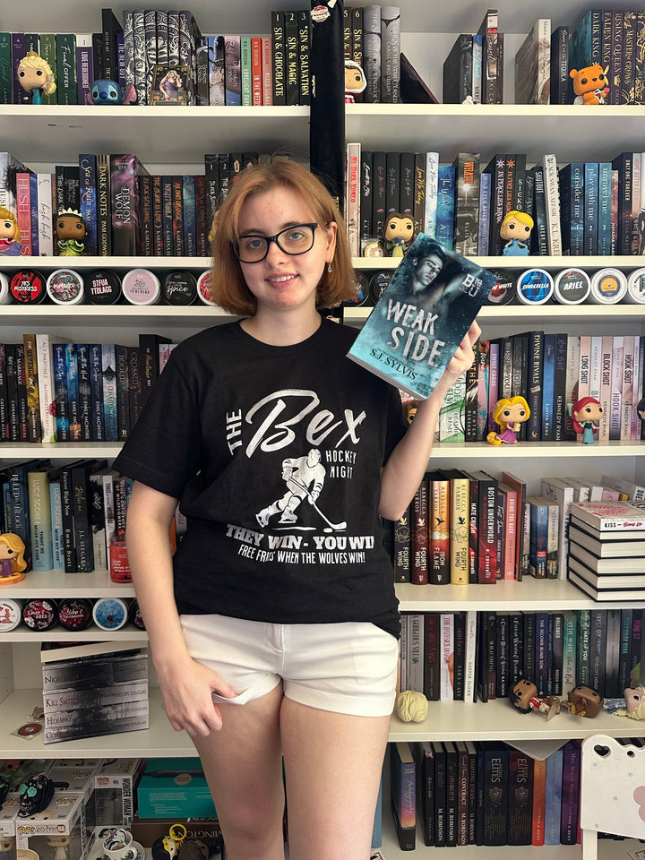a woman standing in front of a book shelf holding a book