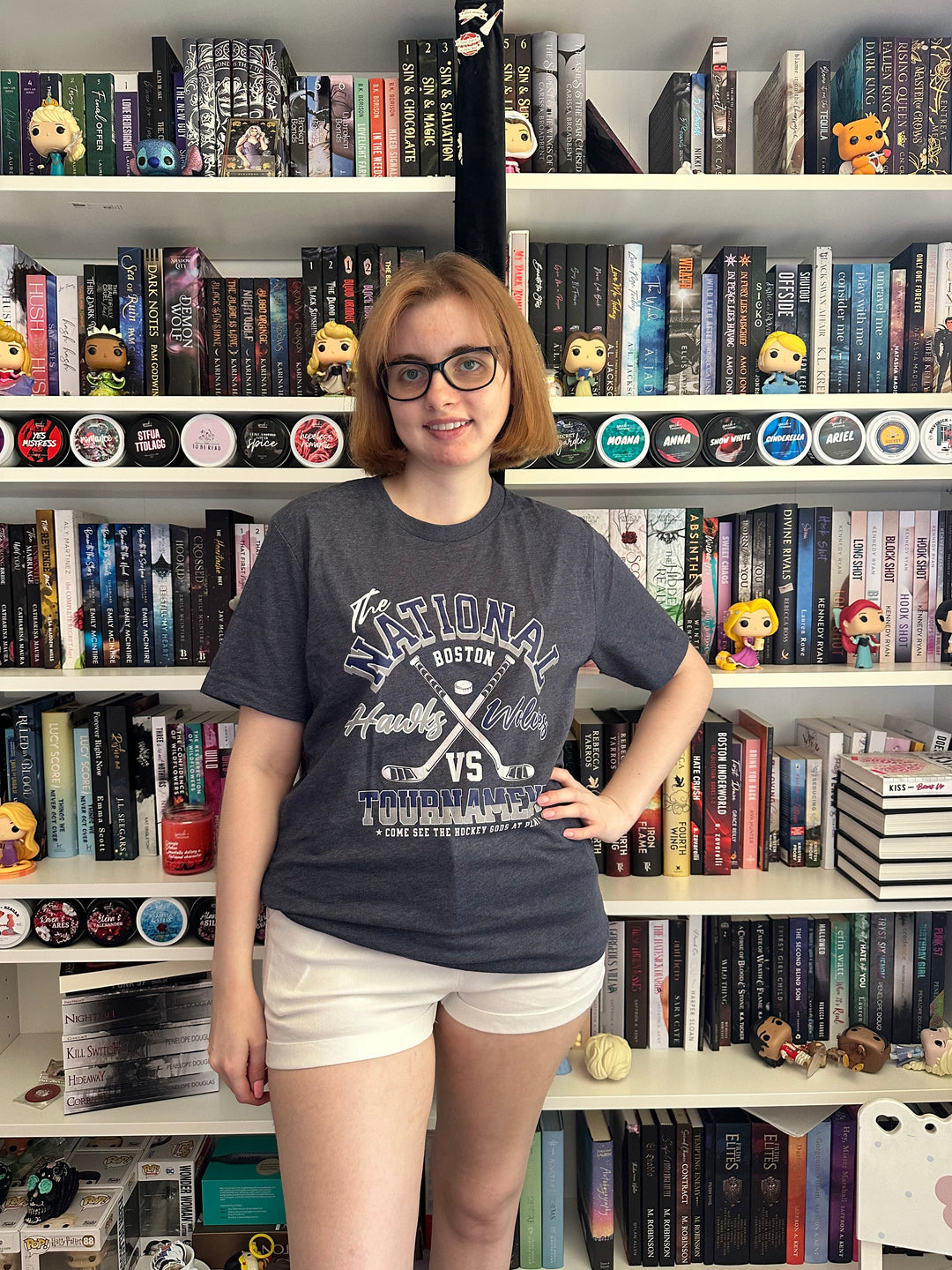 a woman wearing glasses standing in front of a wall of books