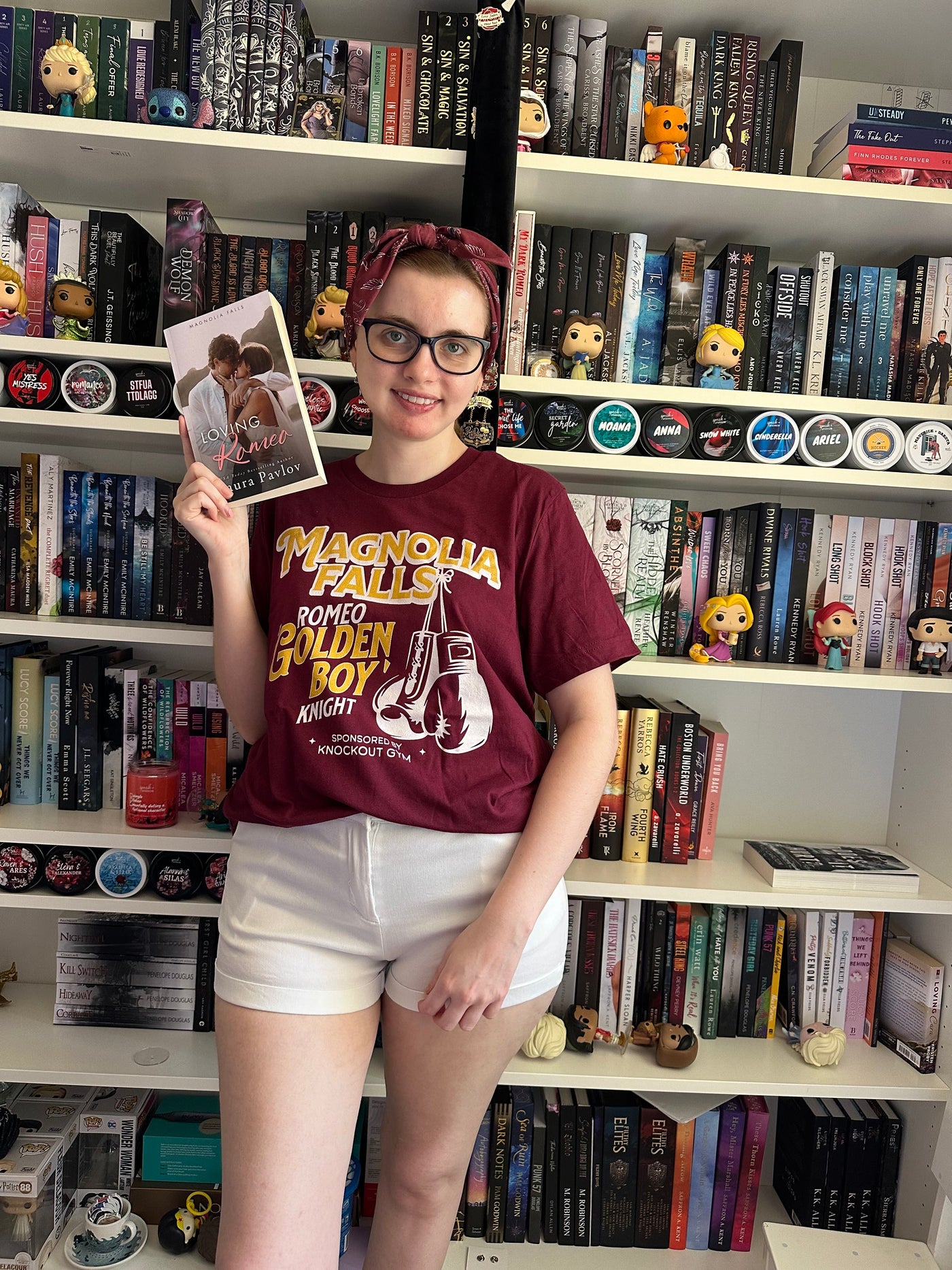a woman in a red shirt and white shorts standing in front of a book shelf