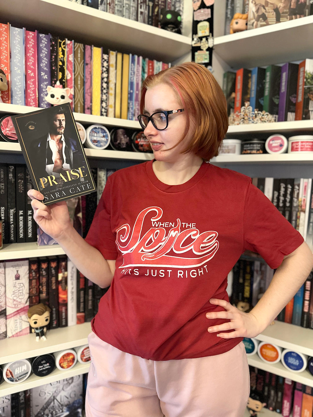 a woman standing in front of a book shelf holding a book